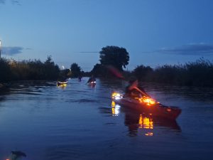 Mit Lichtern geschmückte Kajaks bei der Lampionfahrt in der Abenddämmerung